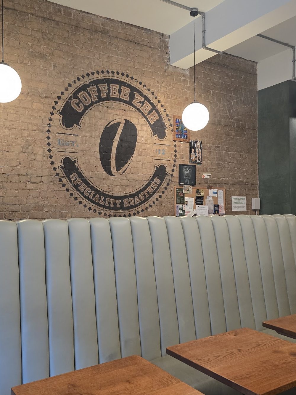Pale green banquette and wooden tables under the painted coffee bean roundel on exposed brick